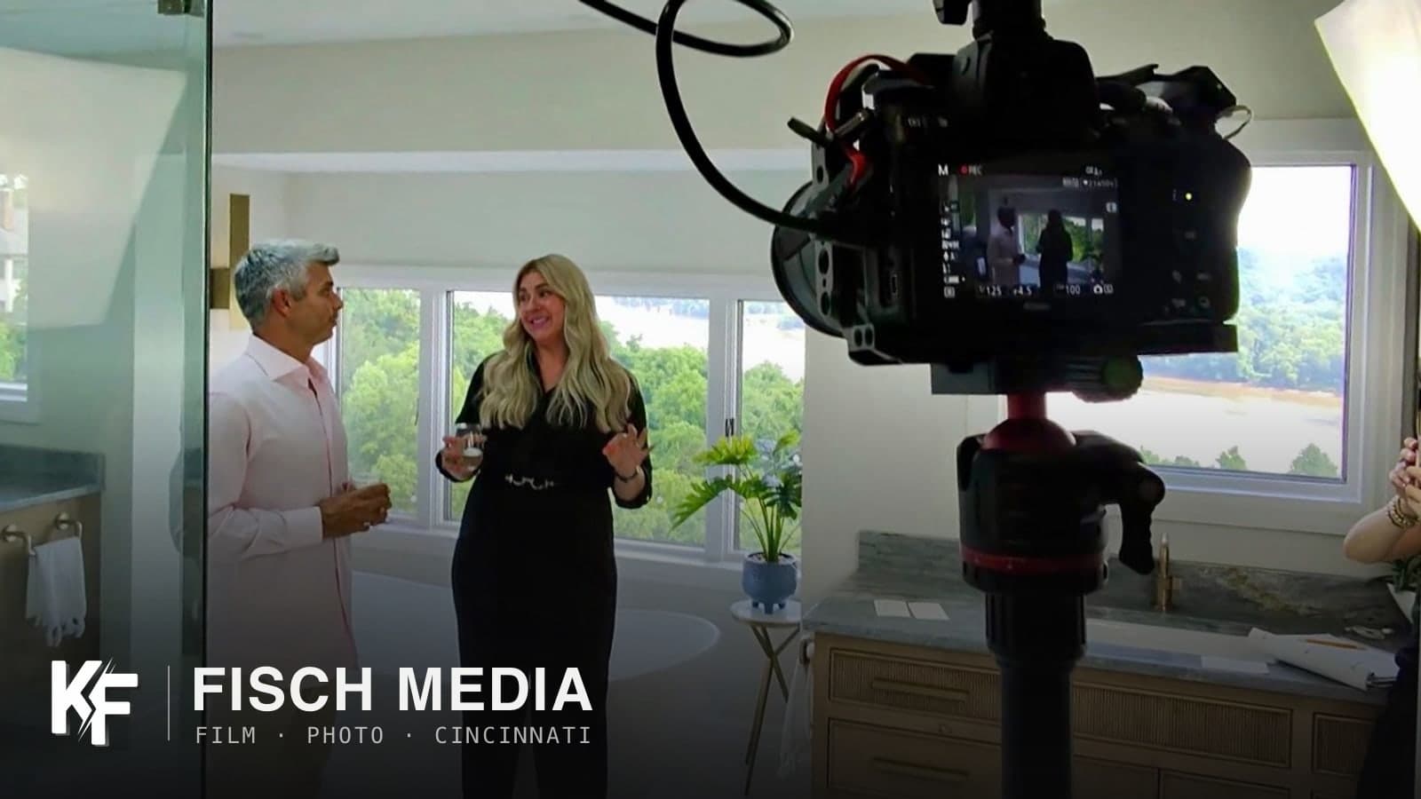Behind the scenes on a bathroom remodel shoot: my camera on a tripod, framing two hosts by the window, with the KF Fisch Media logo